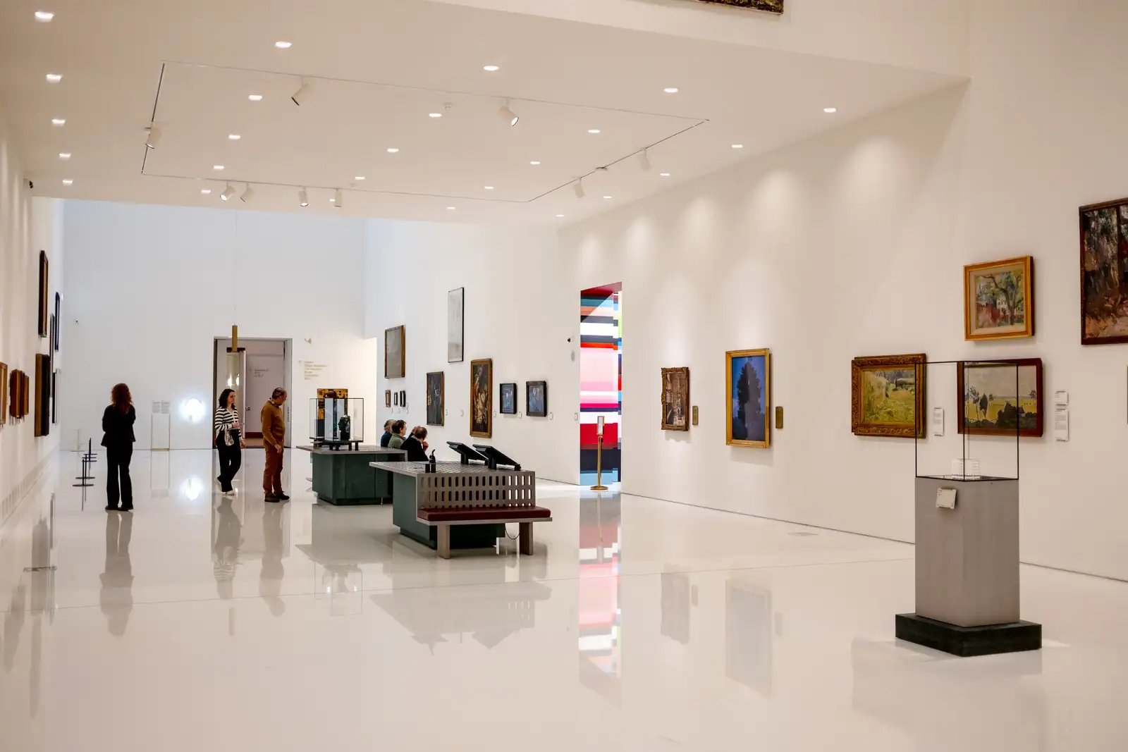 Salle d'exposition d'un musée d'art aux murs blancs, œuvres accrochées et quelques visiteurs.