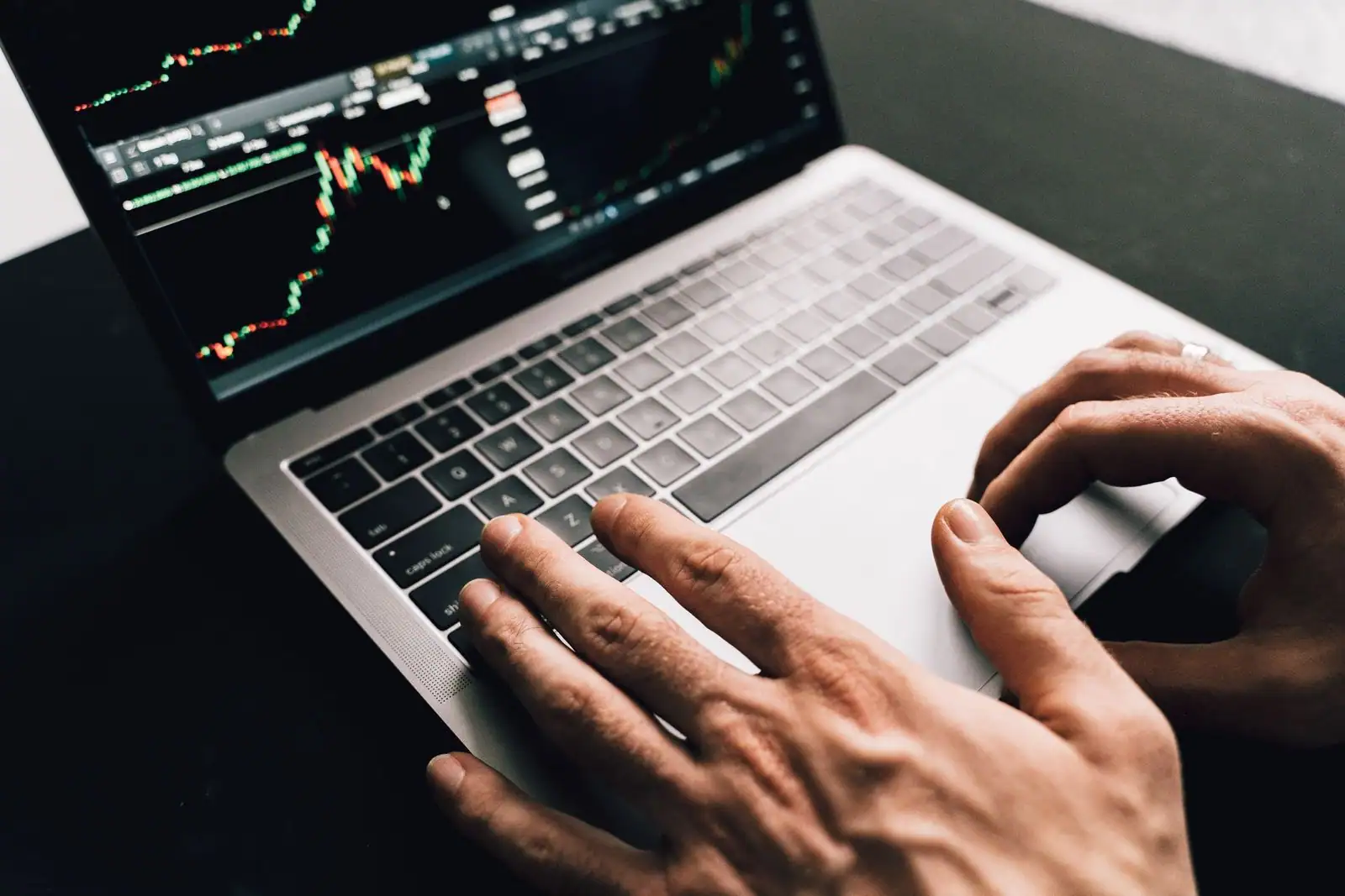 Mains sur le clavier d'un ordinateur portable affichant des graphiques boursiers à l'écran
