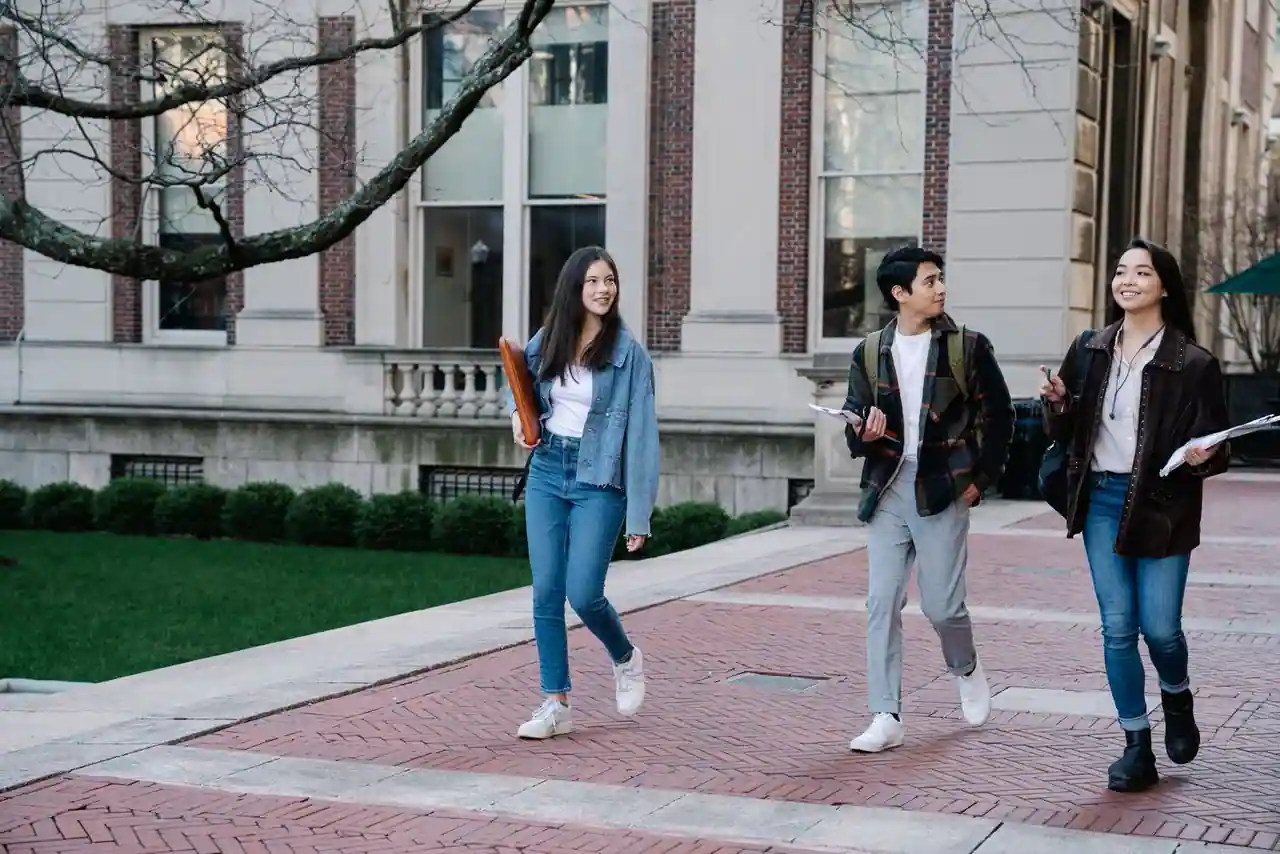 Trois étudiants marchant sur le campus d'une université, des documents et des cahiers à la main
