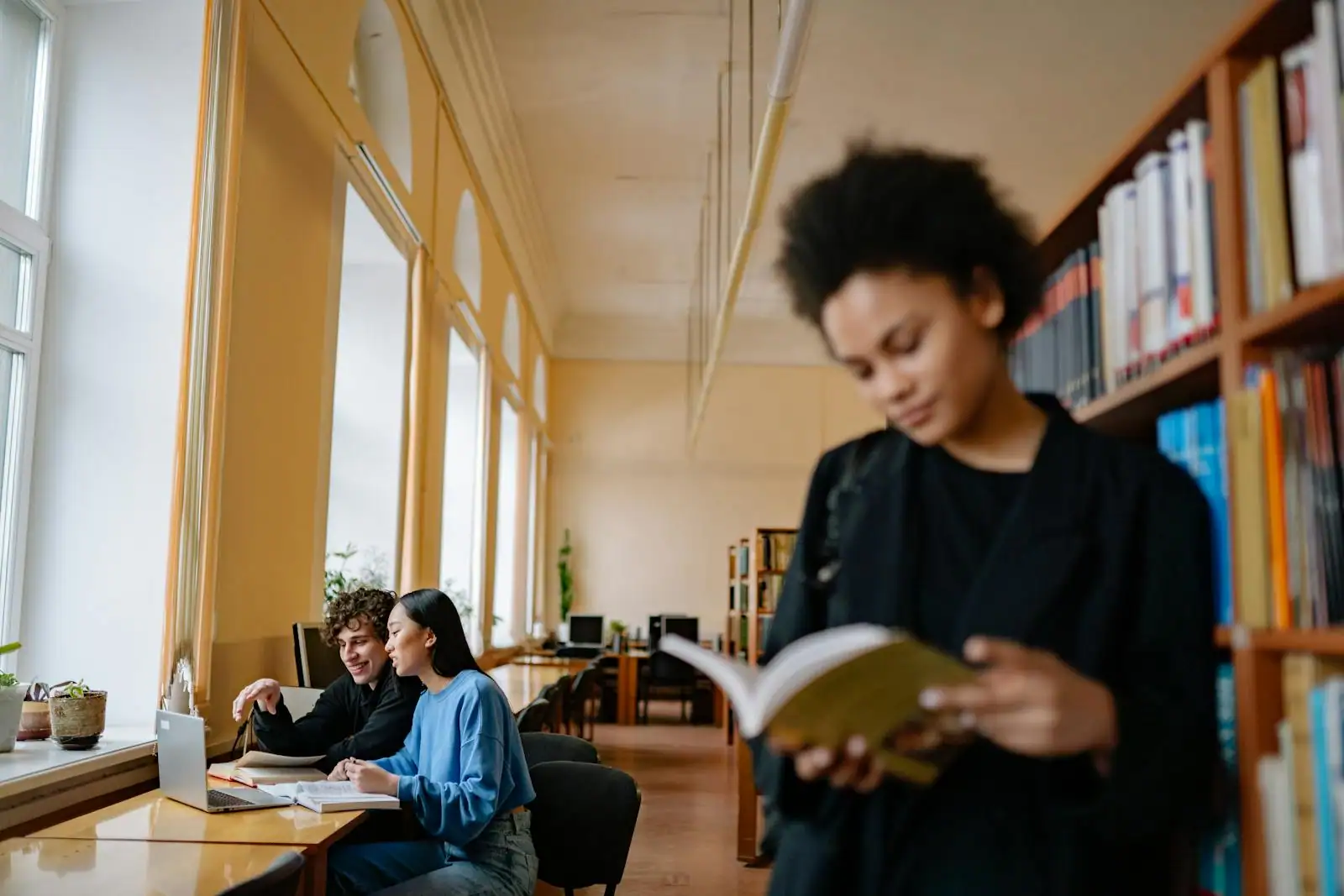 Étudiante souriante révisant avec un ordinateur portable et des livres dans une bibliothèque universitaire.