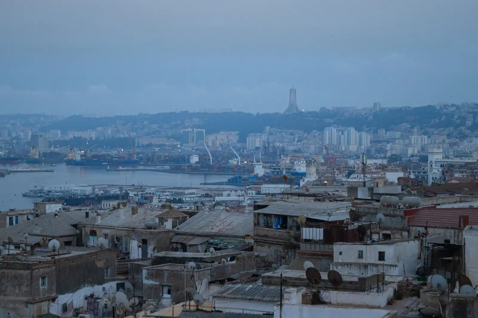 Vue aérienne d'Alger : toits de la ville, baie et port, avec le Mémorial du Martyr en arrière-plan