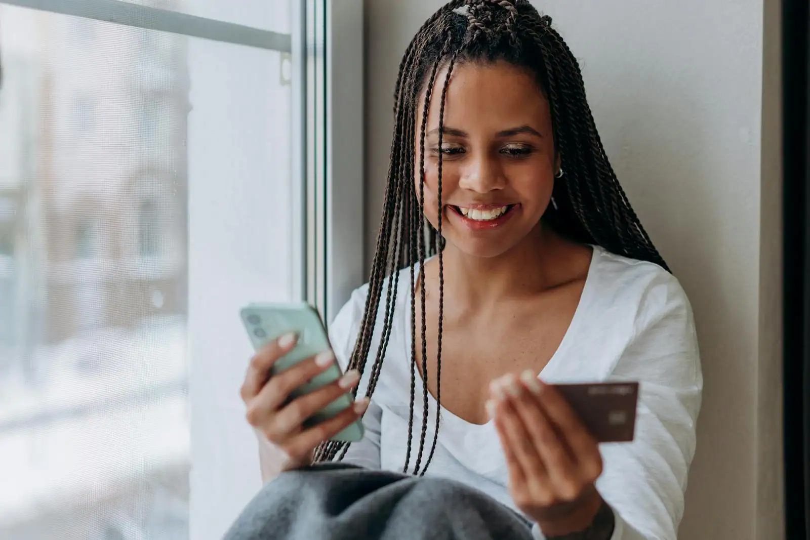 Jeune femme souriante tenant son smartphone et une carte bancaire lors d'un achat en ligne