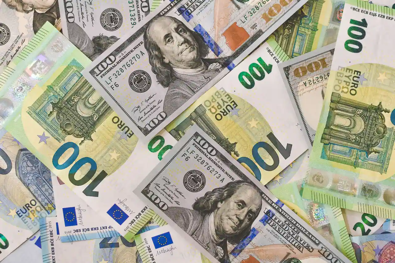 Billets de cent dollars américains et billets en euros mêlés, illustrant le change entre devises.