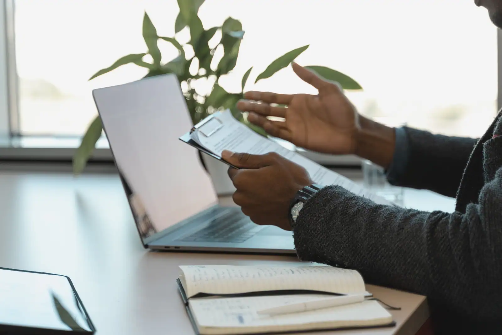 Personne consultant un document papier à côté d'un ordinateur portable ouvert sur un bureau.