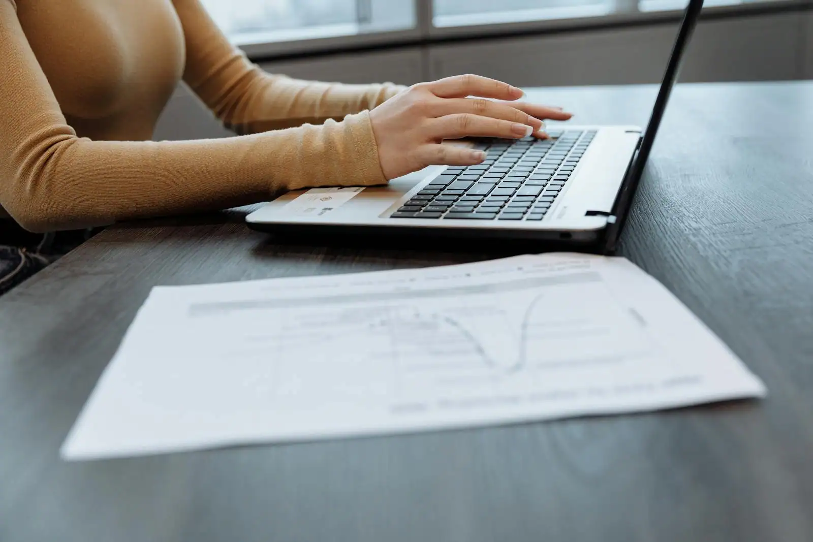 Mains tapant sur un clavier d'ordinateur portable affichant un document bureautique prêt à être enregistré au format PDF.