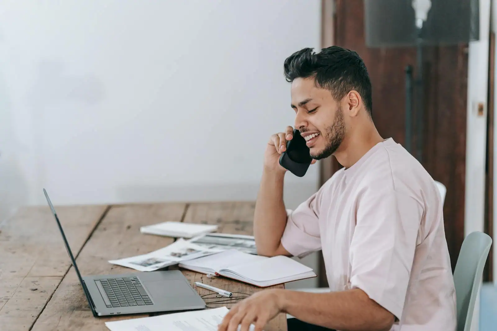 Jeune entrepreneur à son bureau avec un ordinateur portable et des documents, souriant en conversation au téléphone