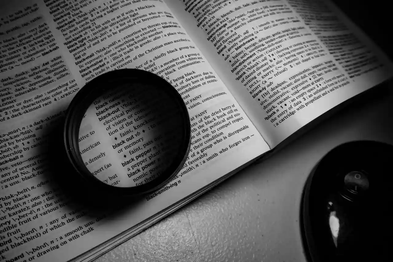 Objectif photo posé sur les pages d'un dictionnaire ouvert, évoquant la recherche du mot juste.
