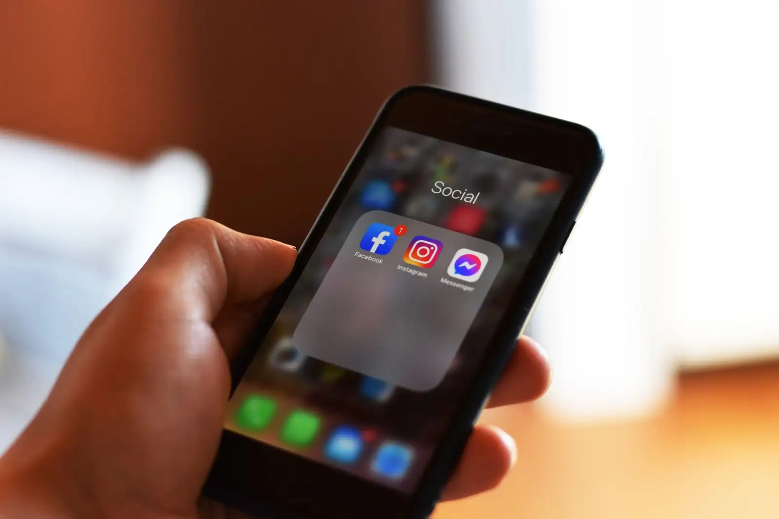 Main tenant un smartphone affichant un dossier d'applications de réseaux sociaux dont Facebook.