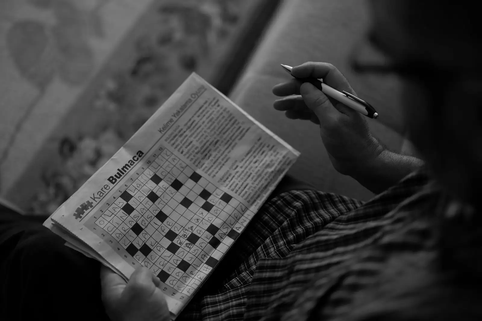 Grille de mots croisés partiellement remplie, stylo à la main, sur une page de journal