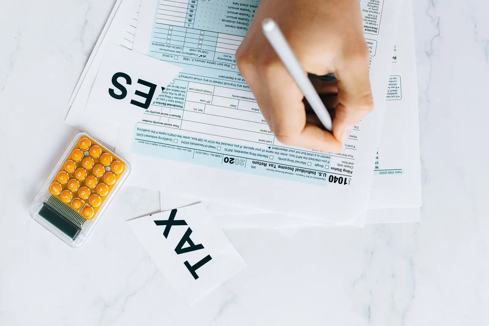 Personne remplissant au stylo un formulaire de déclaration de revenus sur un bureau