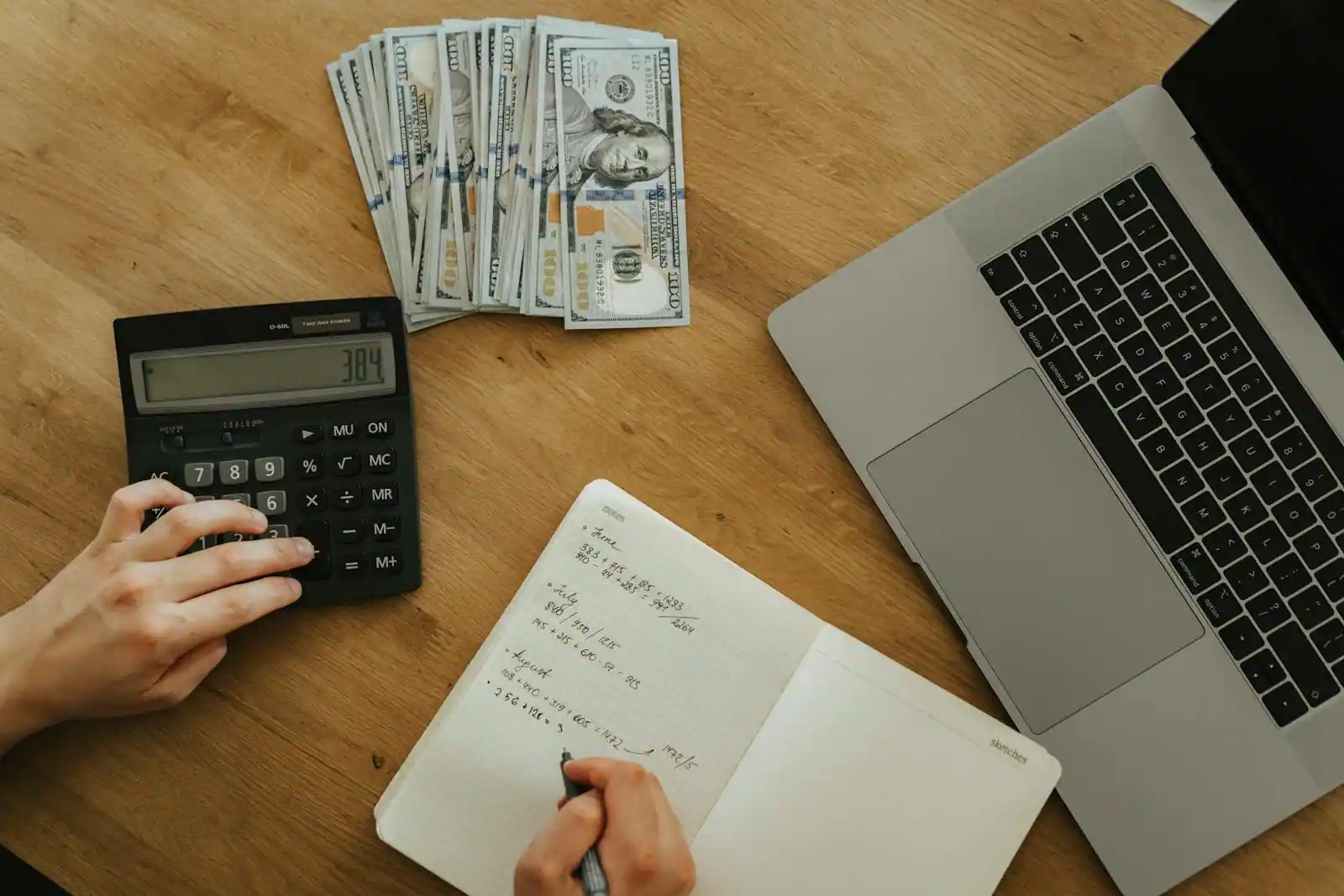 Calculatrice, billets, carnet de calculs et ordinateur portable sur un bureau, illustrant la gestion d'une épargne.