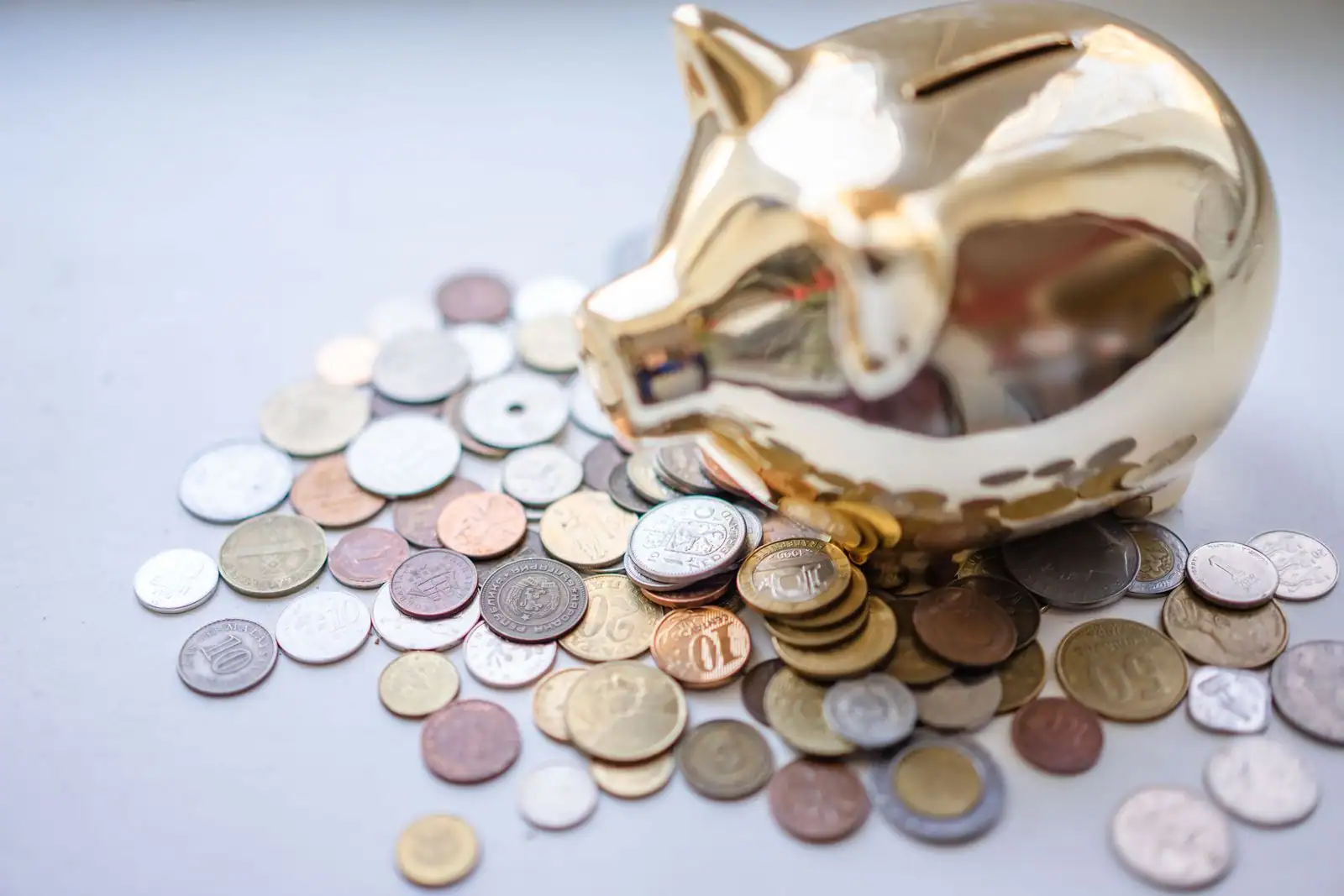 Tirelire dorée entourée de pièces de monnaie sur une surface claire, évoquant l'épargne.