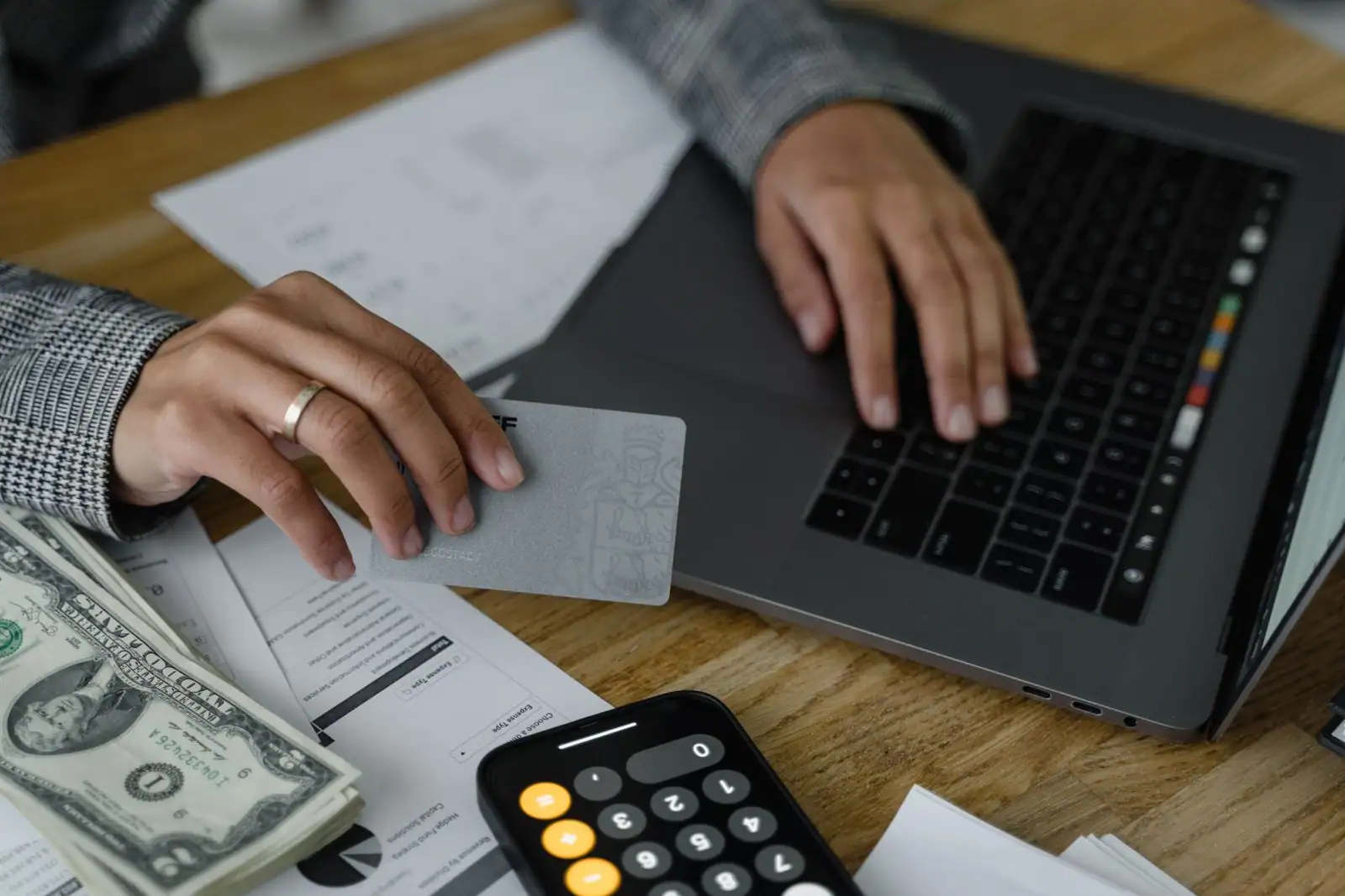 Mains gérant des finances en ligne devant un ordinateur portable, avec carte bancaire, documents et calculatrice.