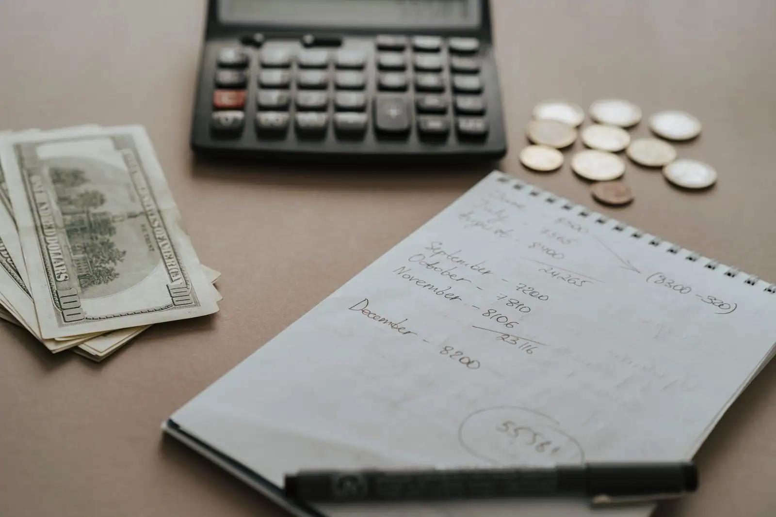 Une calculatrice, des billets, des pièces et un carnet de comptes manuscrit posés sur un bureau