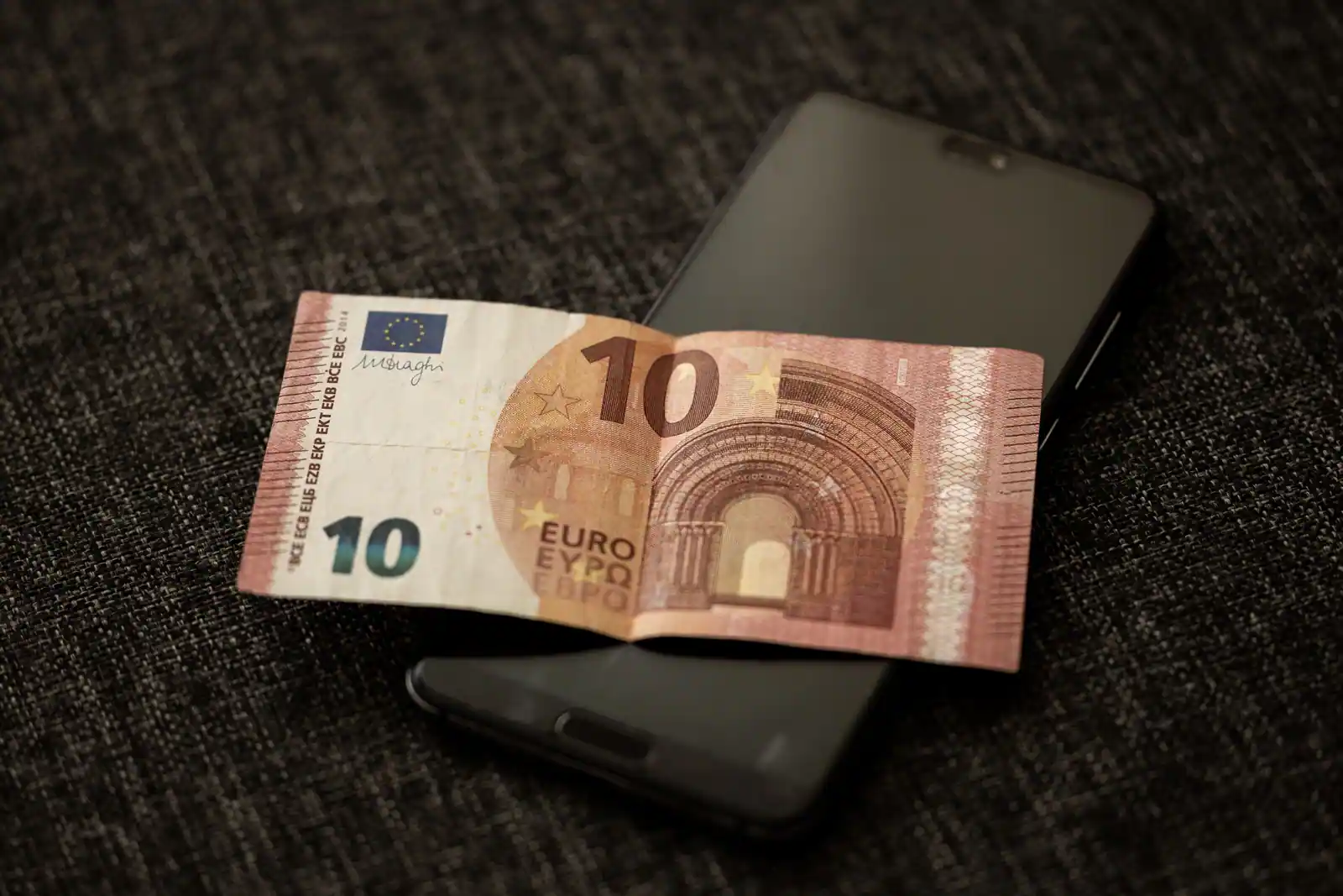 Billet de dix euros posé sur un smartphone, évoquant la gestion bancaire en ligne