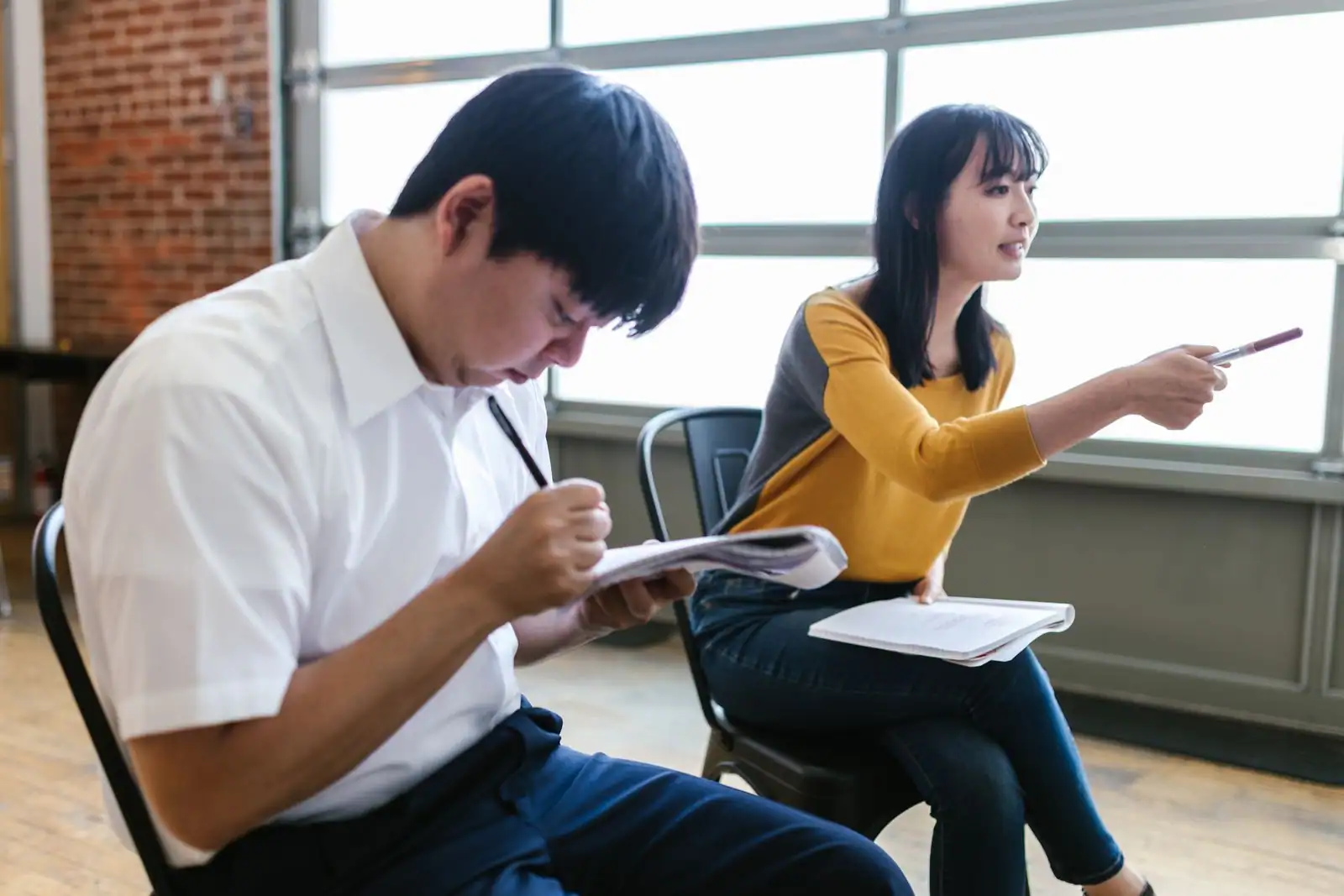Deux adultes assis prenant des notes avec carnets et stylos lors d'un atelier en salle
