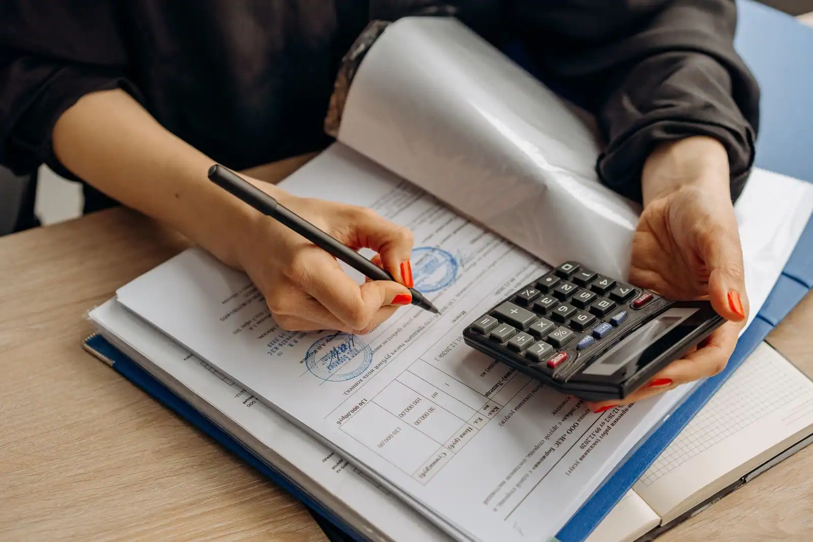 Personne vérifiant des documents financiers avec une calculatrice et un stylo sur un bureau