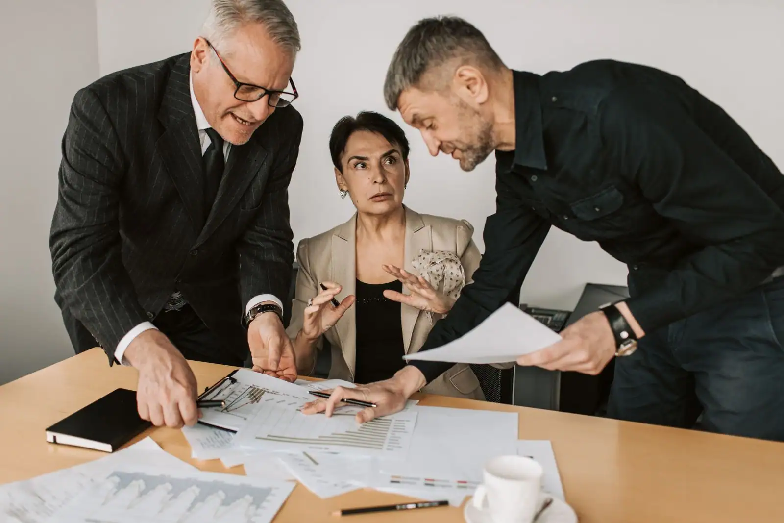 Trois professionnels analysent des documents et des graphiques lors d'une réunion de gestion au bureau.
