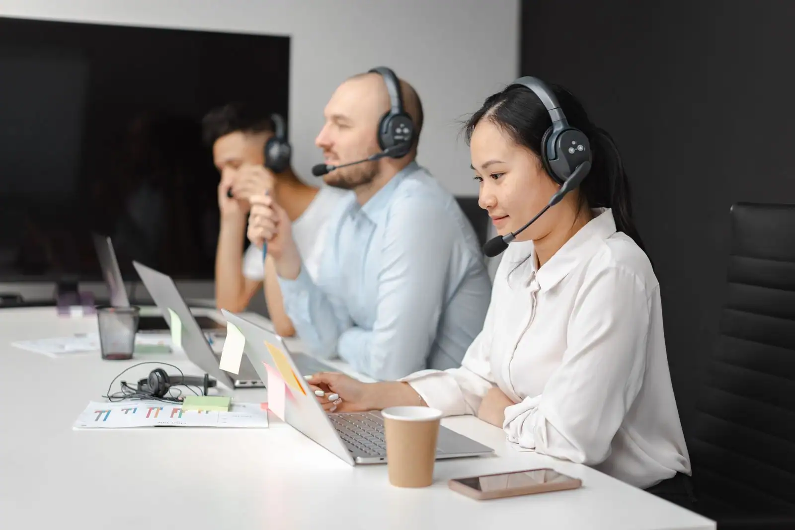 Équipe de service client avec casques audio, au travail sur ordinateurs portables dans un bureau.