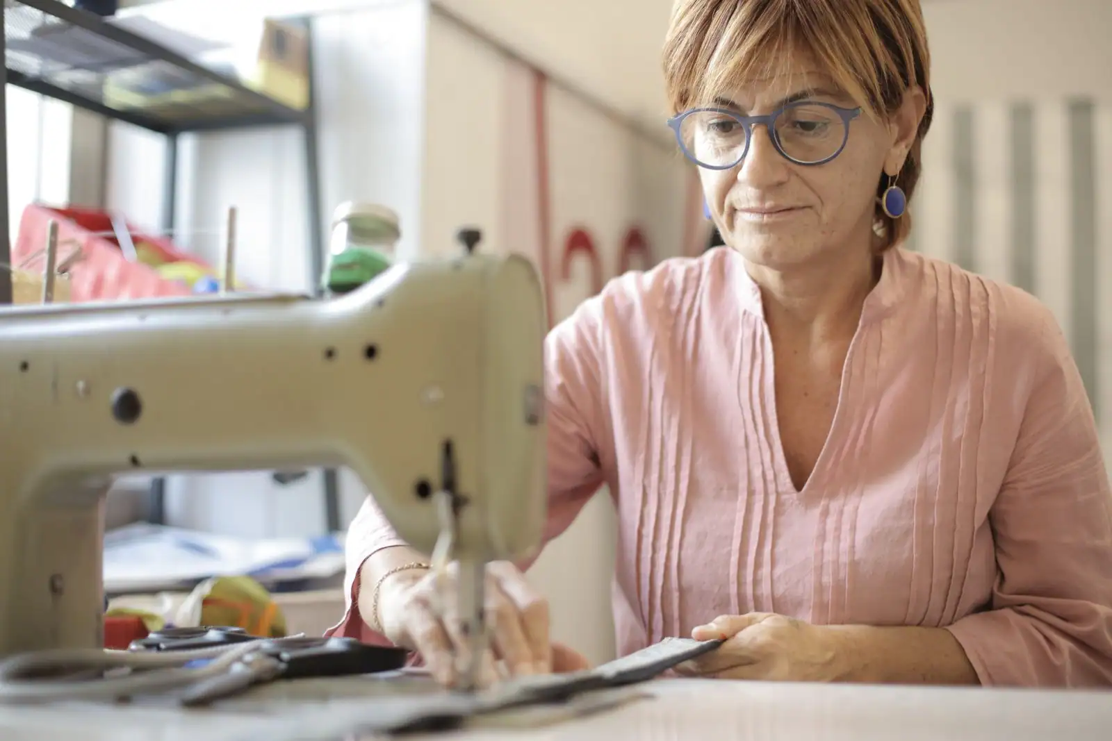 Une femme d'âge mûr concentrée à sa machine à coudre dans un atelier de couture lumineux.