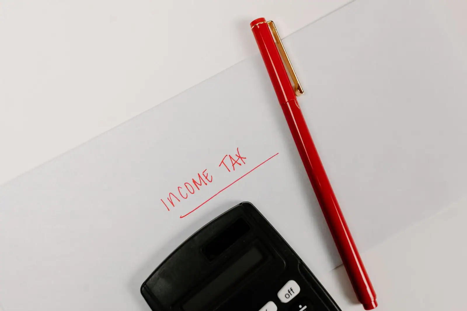Calculatrice et stylo rouge posés sur une feuille évoquant le calcul de l'impôt sur le revenu
