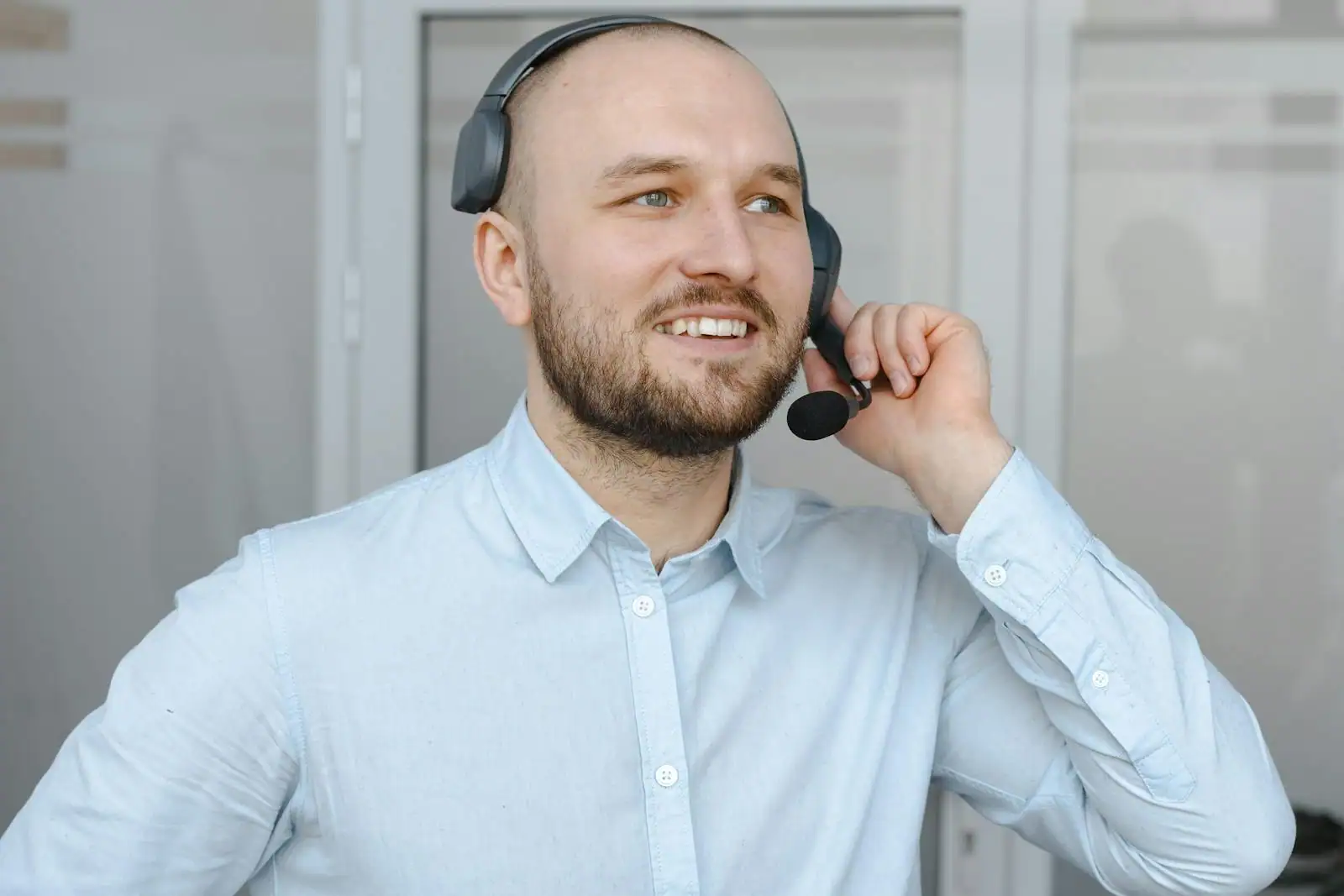 Un homme souriant équipé d'un casque-micro, en chemise claire, dans un environnement de bureau