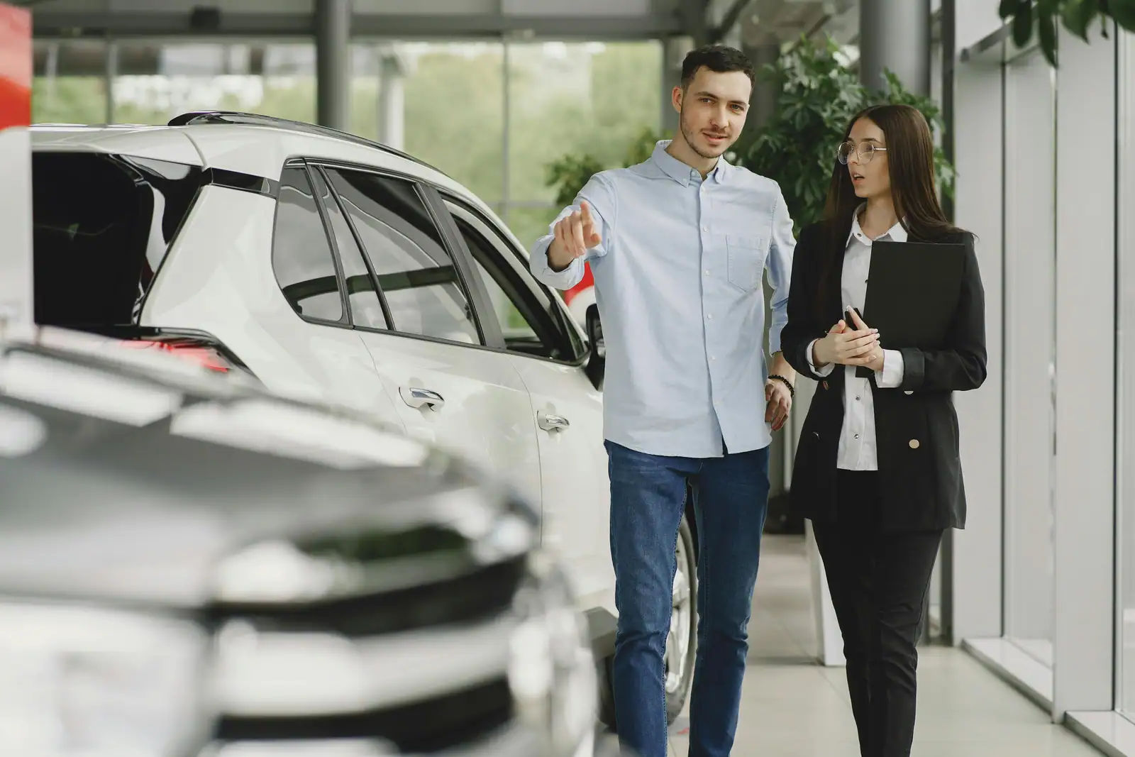 Une conseillère en concession automobile présente un véhicule à un client dans le showroom d'un point de vente.