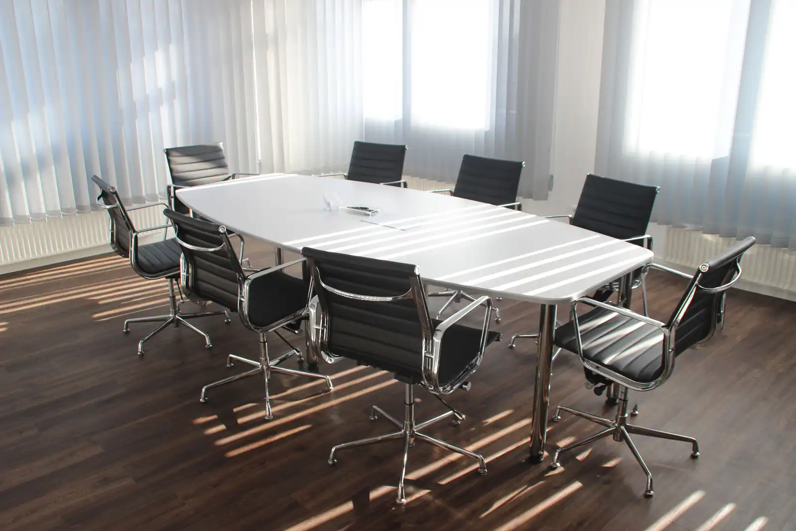 Salle de conseil vide, longue table de réunion blanche entourée de fauteuils de bureau, lumière du jour