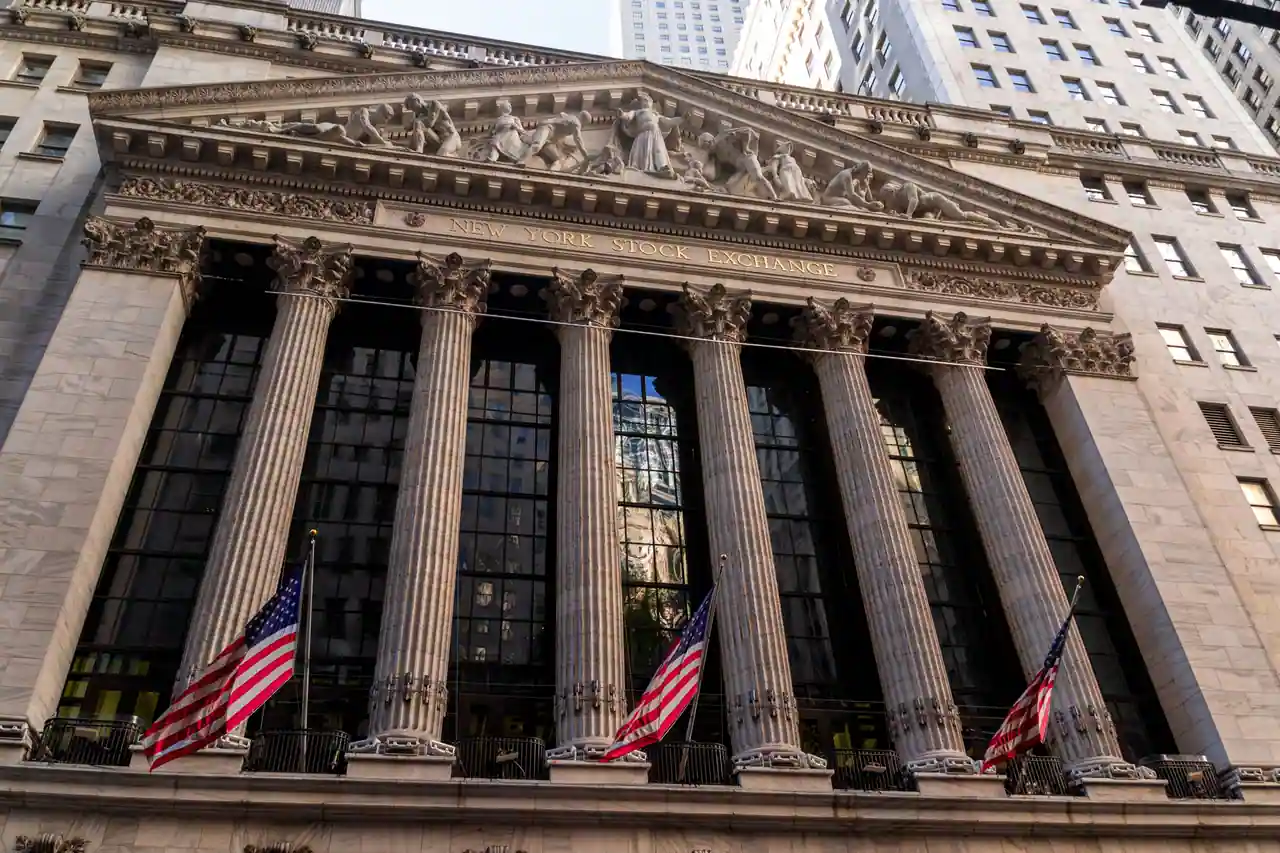 Façade néoclassique du New York Stock Exchange à Wall Street, colonnes et drapeaux américains.