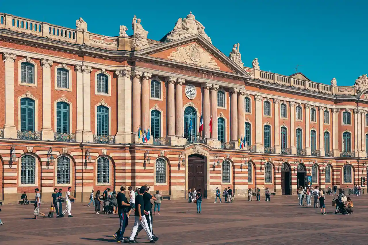 Place du Capitole à Toulouse : la façade de brique rose et des passants en plein soleil.