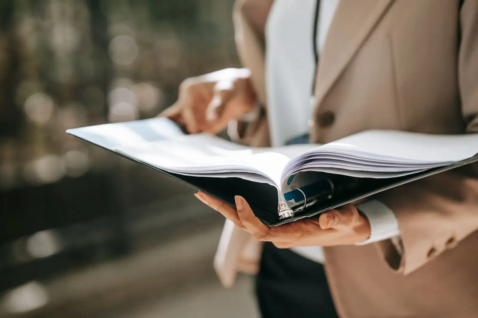 Personne en tenue professionnelle consultant un classeur de documents pour préparer un projet d'entreprise.