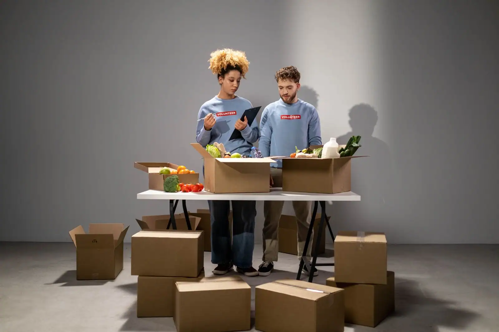 Deux bénévoles en sweat identifié trient des fruits, des légumes et des produits frais dans des cartons de collecte