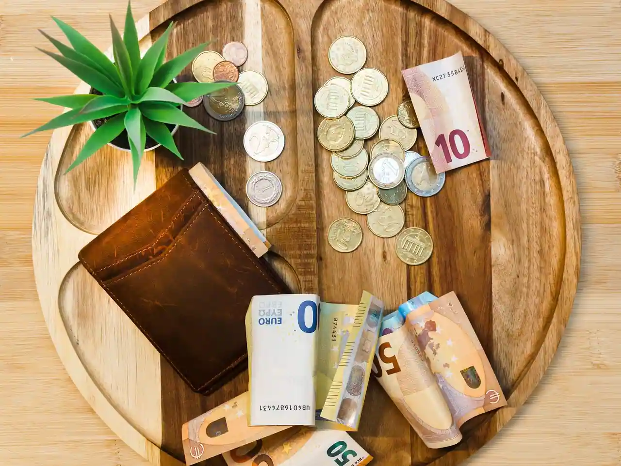 Billets et pièces en euros disposés autour d’un portefeuille en cuir sur un plateau en bois