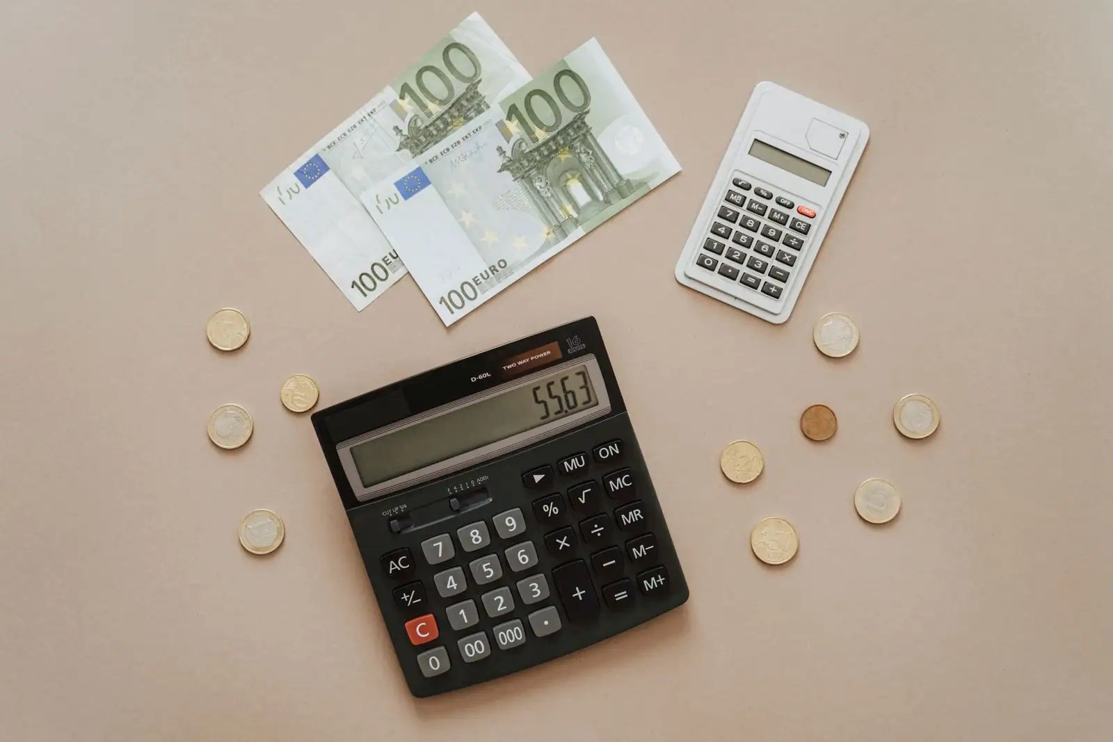 Billets et pièces en euros disposés autour de deux calculatrices, dont l'une affiche un résultat de calcul