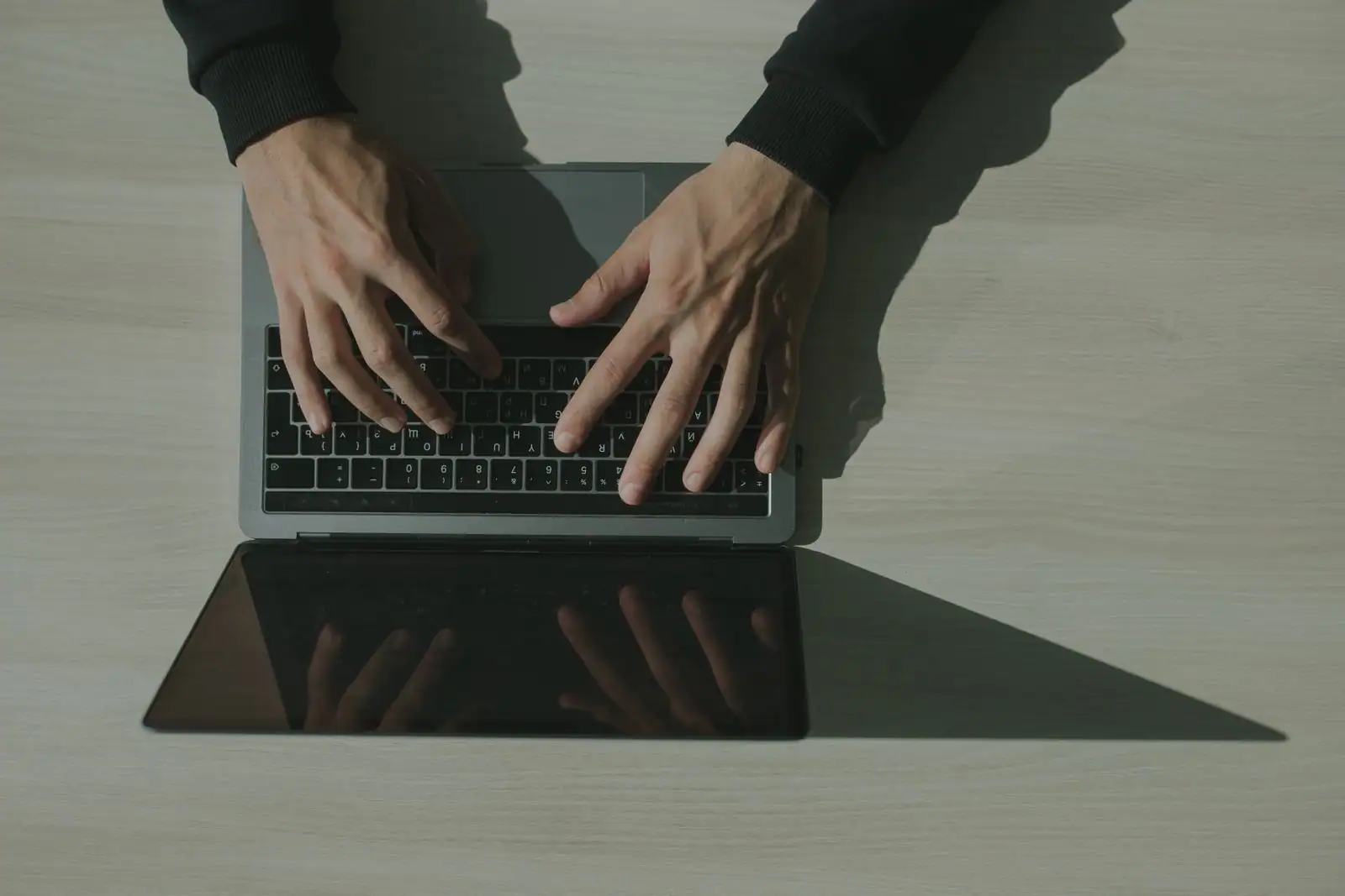Vue de dessus de deux mains en train de taper sur le clavier d’un ordinateur portable posé sur un bureau clair