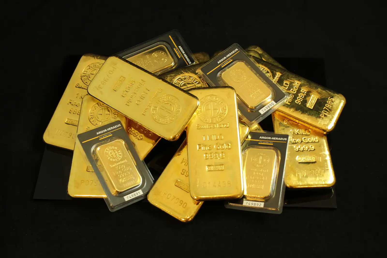 Lingots et lingotins d'or d'investissement empilés, certains scellés sous blister, sur fond noir