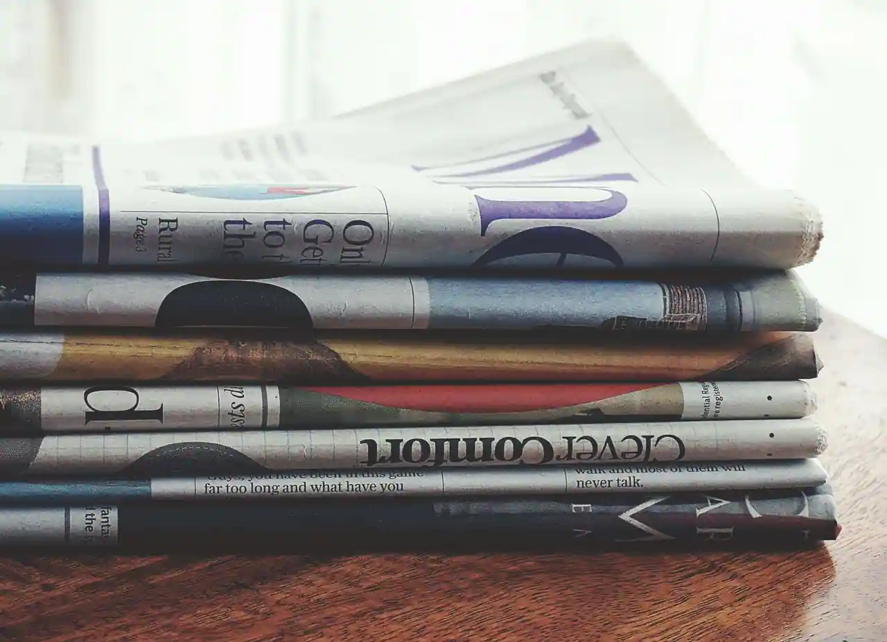 Pile de journaux pliés sur une table en bois, plusieurs titres de presse écrite superposés