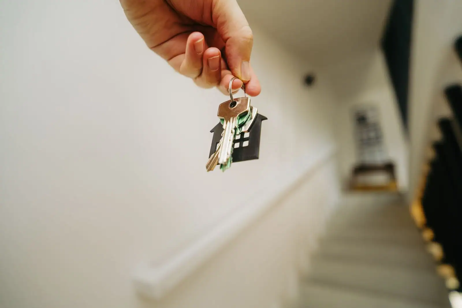 Une main tient un trousseau de clés avec un porte-clés en forme de maison, devant un escalier