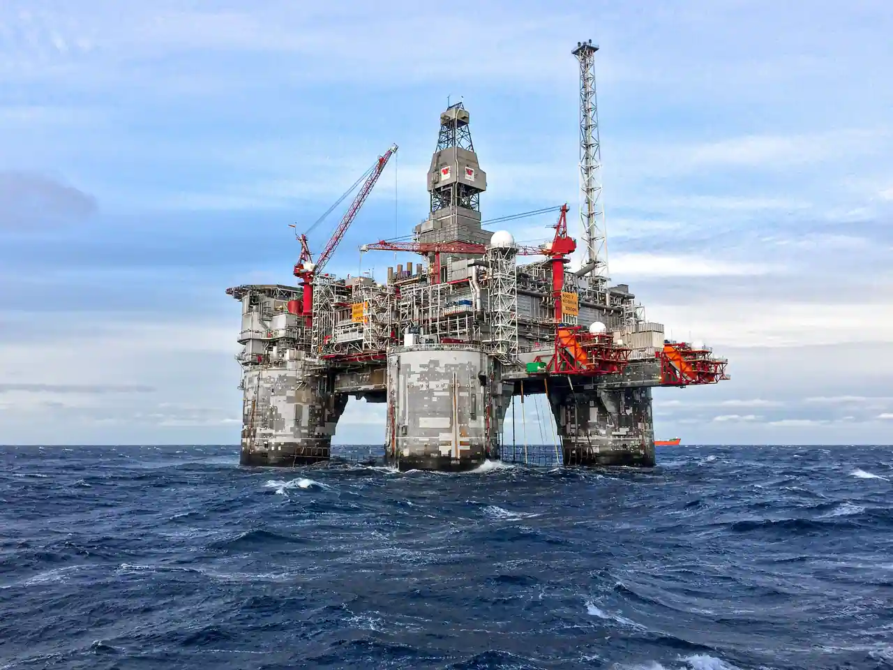 Plateforme pétrolière fixe en pleine mer, tour de forage, grues et torchère dressées au-dessus de la houle.
