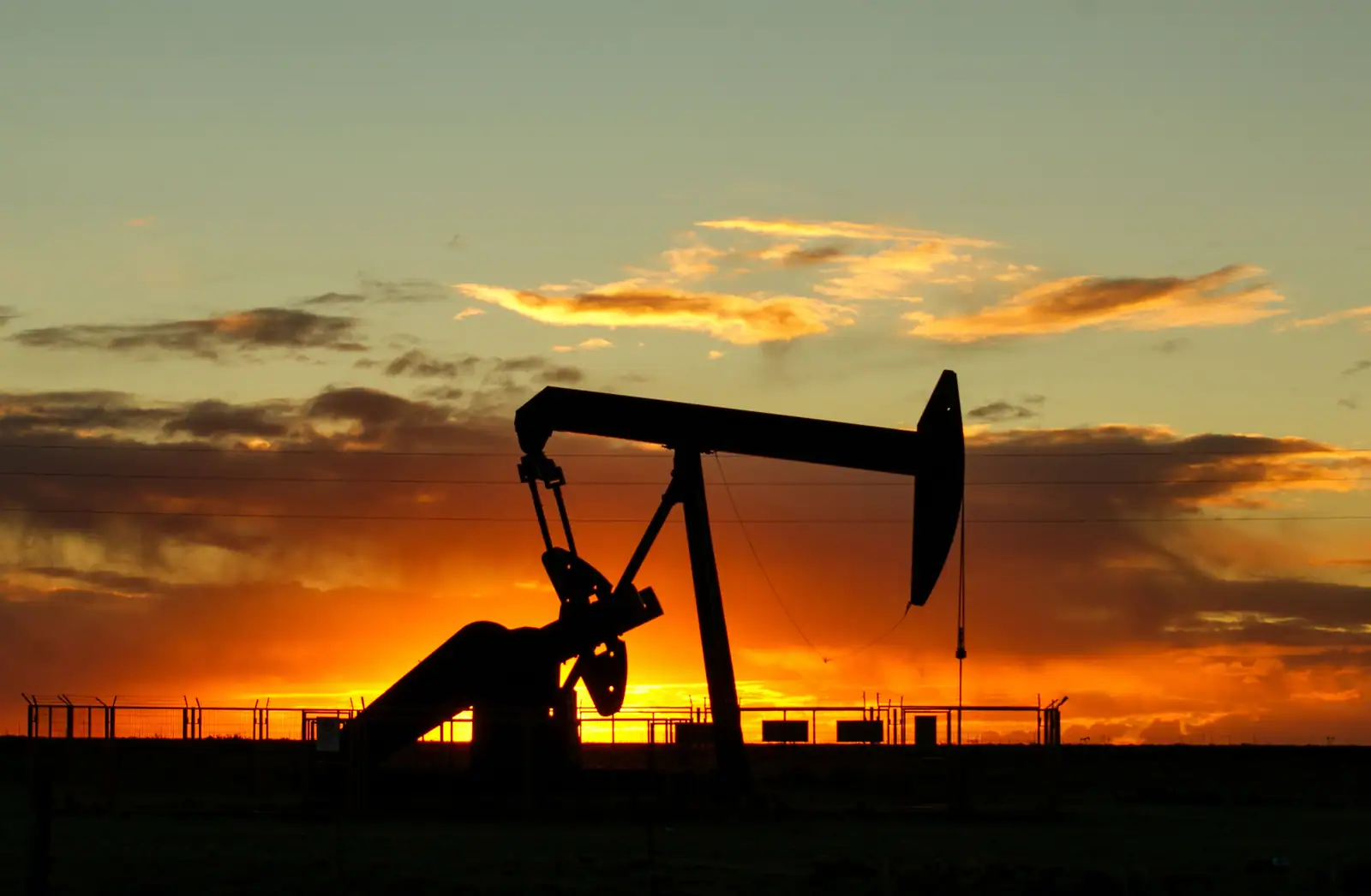 Pompe à pétrole en silhouette devant un ciel de coucher de soleil orangé.
