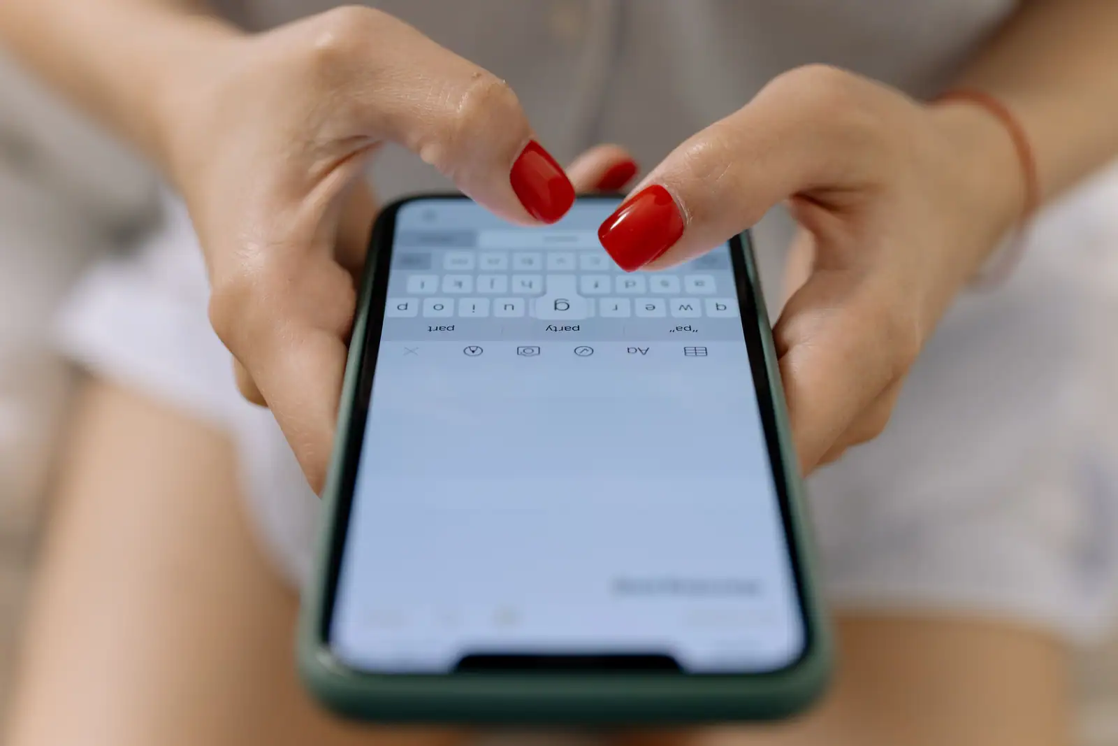 Une personne tape sur l'écran tactile de son smartphone, mains en gros plan sur le clavier
