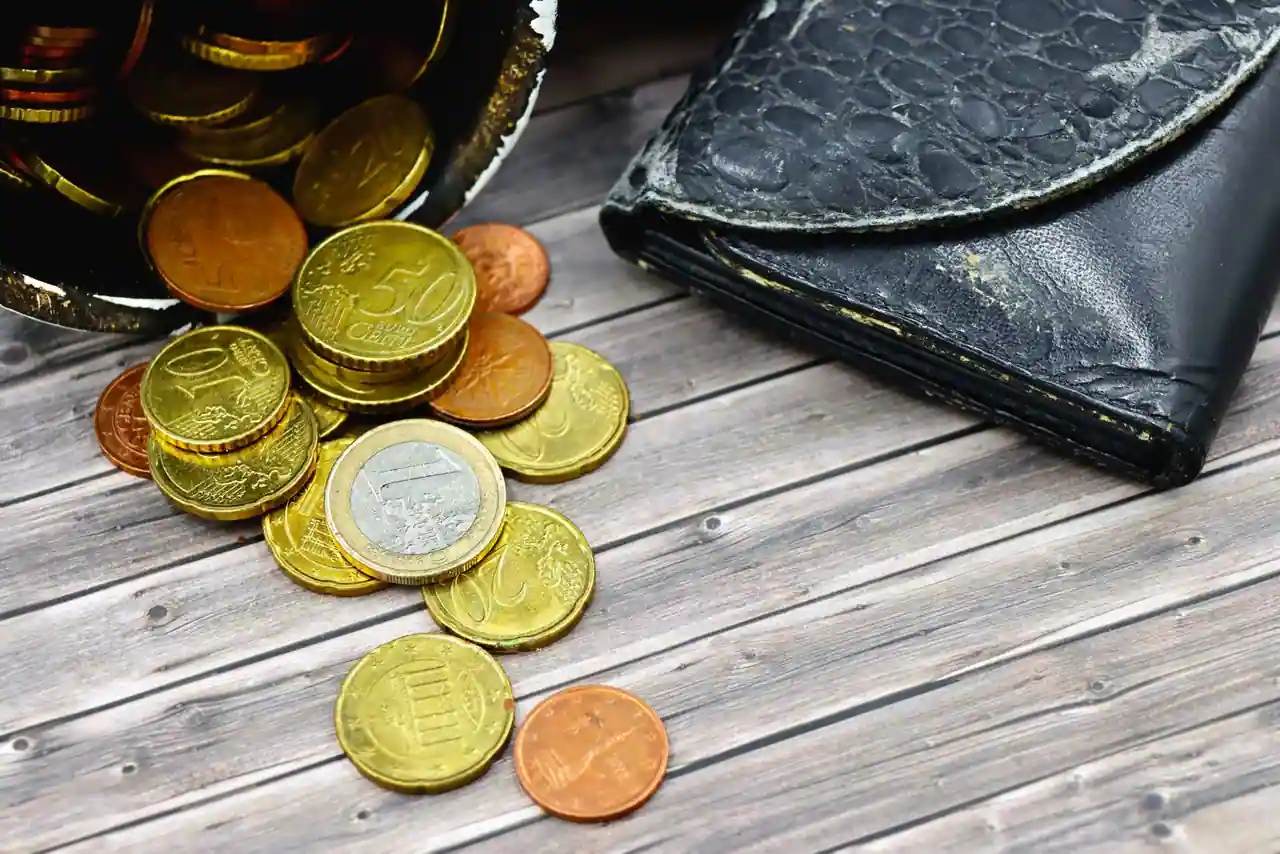Pièces d'euros de différentes valeurs éparpillées près d'un portefeuille en cuir, sur une table en bois