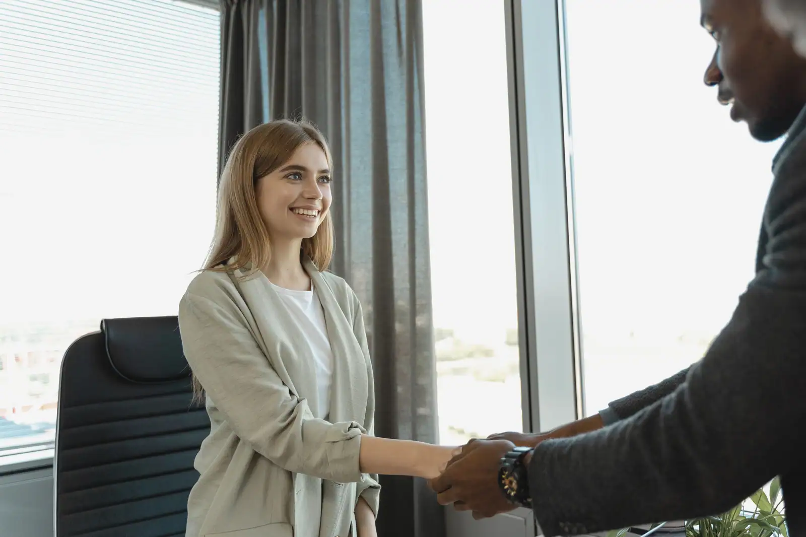 Une candidate souriante serre la main de son recruteur dans un bureau lumineux.